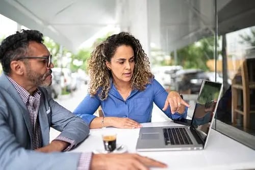 Pessoas sentadas em frente a um notebook. A imagem sugere que eles estão discutindo sobre algo apresentado na tela, trabalhando em conjunto.