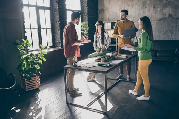 Na imagem, um grupo de quatro pessoas, dois homens e duas mulheres, todos jovens e brancos, vestem roupas casuais. Estão ao redor de uma mesa em um escritório, conversando sobre um projeto. O tema do artigo são as avenidas de crescimento.