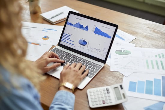 A imagem mostra uma moça sentada em frente a notebook e no visor há dashboards. Ela está analisando esses dados.