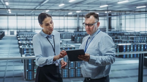 A imagem apresenta um homem e uma mulher em um data center. O tema do artigo é gêmeos digitais.