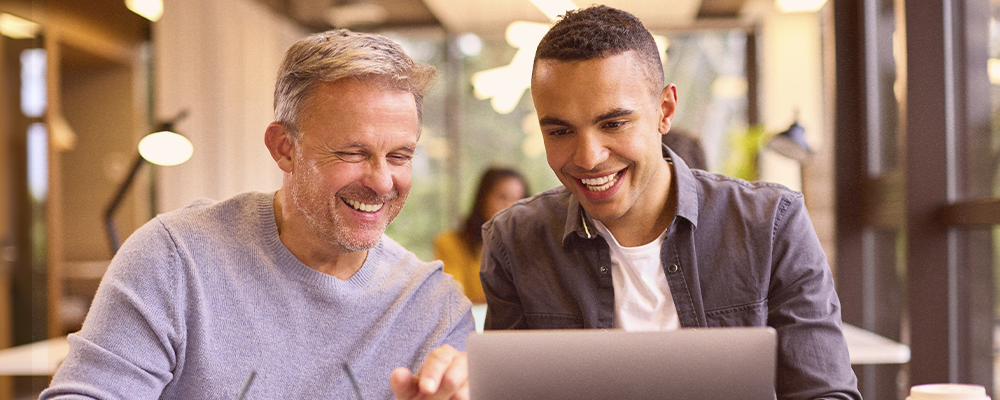 Um homem mais velho, experiente no ramo corporativo, conversando com um jovem que está adentrando o mercado.